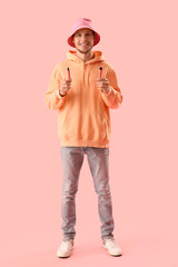 Young man in bucket hat with disposable electronic cigarettes on pink background