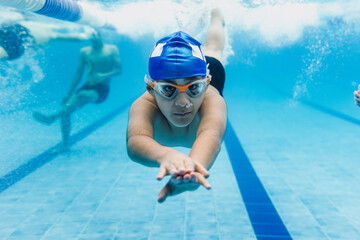 latin child boy swimmer wearing cap and goggles in a swimming underwater training In the Pool in...