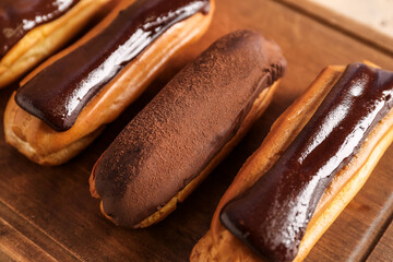 Wooden cutting board with tasty chocolate eclairs, closeup