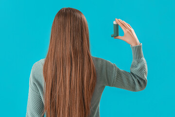 Young woman with inhaler on blue background, back view