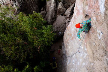 A male climber in an orange beanie and multicolored shirt climbs Family Jewel (5.10d) on Mount Gorgeous in Malibu Canyon State Park in Malibu, California.  Family Jewel is a very p