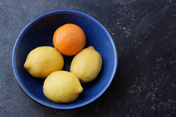 Lemons and an orange in a blue bowl.