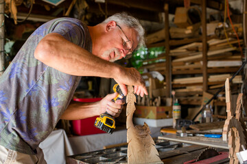 A craftsman leans over his work to drill