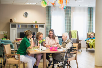 Senior women with girl and nurse doing craft activity at rest home
