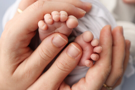 Small feet of a newborn in the hands of parents. Loving palms of the hands of mother. Conceptual image of fatherhood. Close-up, selective focus. Professional photography a white background.