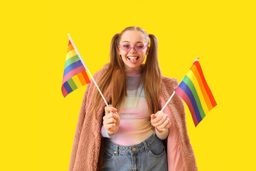 Young woman in sunglasses with LGBT flags showing tongue on yellow background