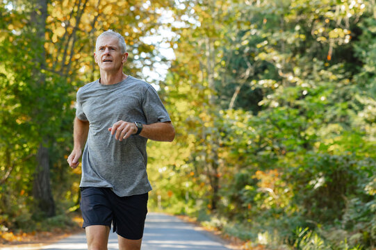 Runner jogging easily on paved road in the trees.