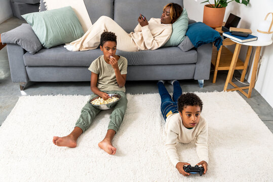 Mother and two sons watching the youngest playing videogame