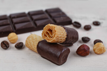 Delicious wafer rolls, nuts, coffee beans and chocolate on light table, closeup