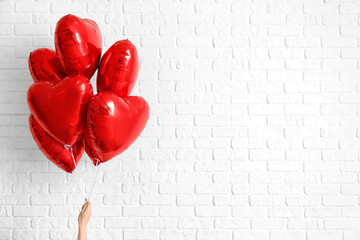 Woman with heart shaped balloons for Valentine's Day on white brick background