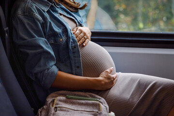 Midsection of pregnant woman sitting by window in train