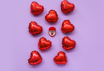 Box with ring and red foil balloons on lilac background. Valentine's Day celebration