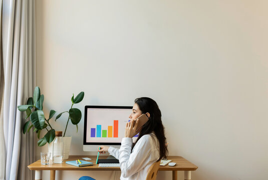 Freelance Woman Making Phone Call At Home Office Desk
