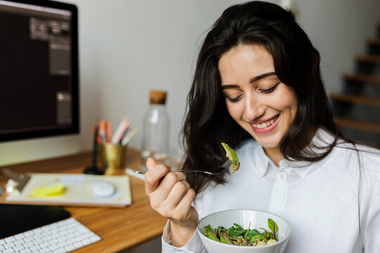Cheerful freelancer woman eating salad from her desk