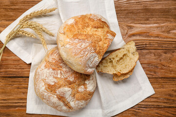 Napkin with loaves of fresh bread and wheat ears on wooden background