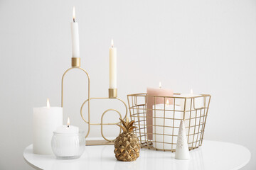 Candle holders with burning candles and decorative golden pineapple on table near white wall