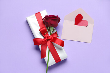 Gift box with beautiful bow, rose flower and envelope on lilac background. Valentine's Day celebration