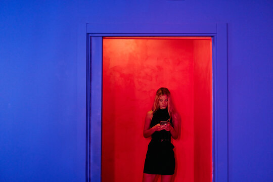 Young woman browsing smartphone on red room