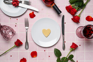 Table setting with bottle of wine, rose flowers, petals and glasses on pink tile background....