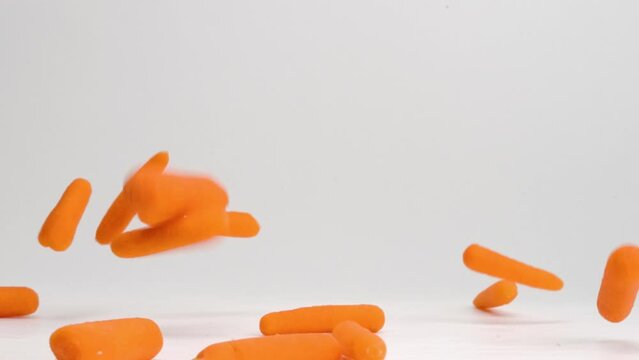 Bright orange baby carrots raining down onto white table top and bouncing in all directions in slow motion