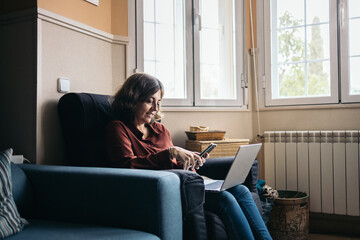 Mature woman using laptop and smartphone at home