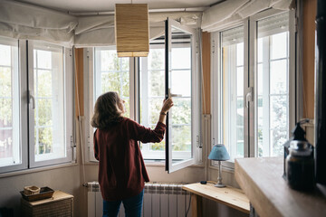 Middle-aged woman opening the window at home