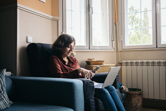 Mature woman using laptop and smartphone at home