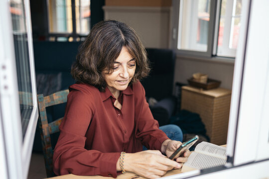 Woman interrupting her reading to use smartphone at home