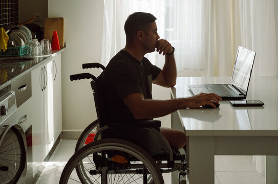 Adult man in a wheelchair reading news on a laptop