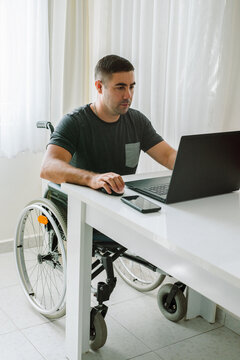 Adult man in a wheelchair reading news in a laptop