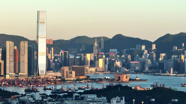 High skyline of Hong Kong city illuminated by the setting sun among the high mountains of green nature. Zoomed drone shot