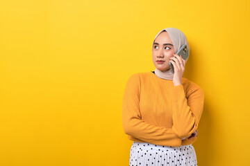 Beautiful pensive Asian girl wearing hijab talking on cell phone, serious face thinking question...