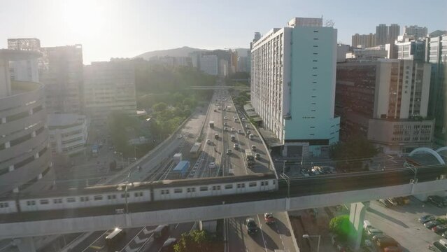 Backwards shot of busy highway revealing trains passing on overpass. Drone pull-away shot, facing sun.