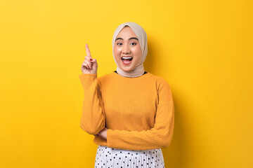 Excited beautiful Asian girl wearing hijab having creative idea, pointing finger up at copy space isolated on yellow background - obrazy, fototapety, plakaty