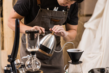 Fototapeta na wymiar Professional coffee maker - Barista using coffee siphon brewing hot espresso at coffee shop coffee brewing syphon alternative method. Startup Business Concept.