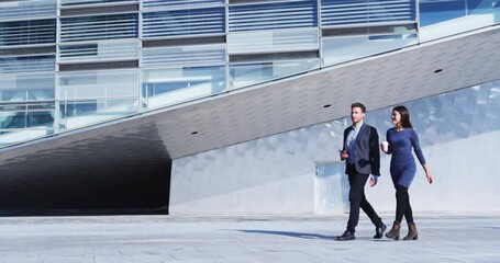 Business people walking and talking - businessman and businesswoman outdoors by office building. Young professional business woman and business man in smart casual clothing. SLOW MOTION - Powered by Adobe