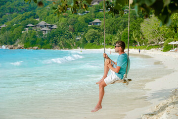 Young men relaxing in a swing on the beach of Mahe Tropical Seychelles Islands. 