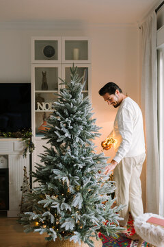 A man dressed in comfy clothes decorating a Christmas tree