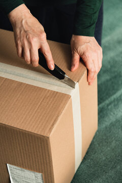 Middle-aged adult woman opening clothing delivery box using cutter