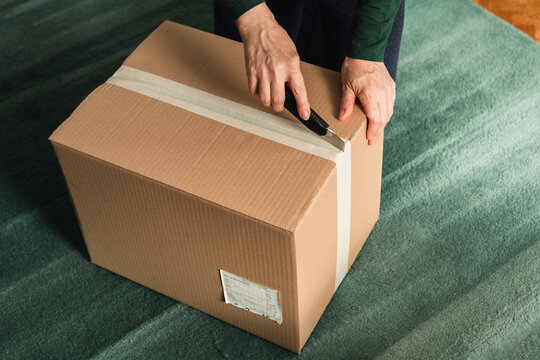 Middle-aged adult woman opening clothing delivery box using cutter