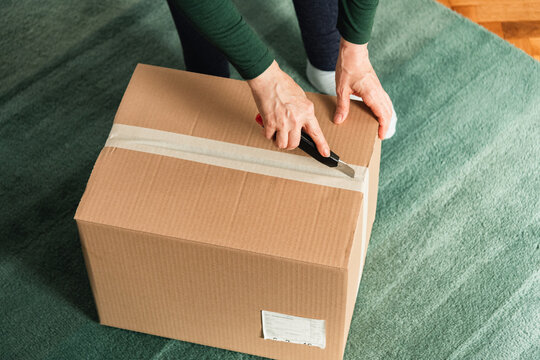 Middle-aged adult woman opening clothing delivery box using cutter