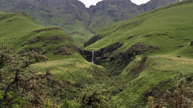 Water falls off vibrant green grassy Lesotho plateau in Sani Pass