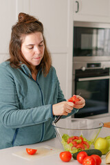 long-haired brunette girl cutting tomatoes to prepare a salad in her home kitchen