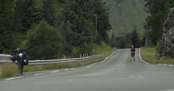 Young caucasian male skateboarder trying and failing on a kickflip on a remote road in Norway, scandinavia. Clearly annoyed, but skating back to try again. Static long lens shot.