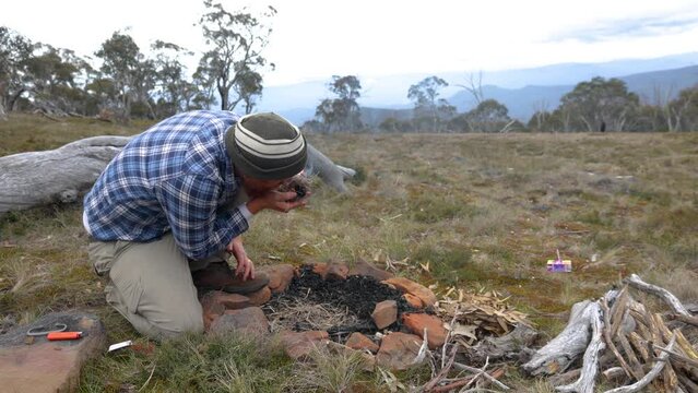 A man blows on a tinder buddle to get a fire going in the Australian mountains.