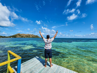 person on the back facing the blue sea raising his arms
