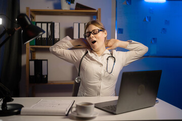 Fototapeta na wymiar Tired medical doctor woman yawning in office duty at night.
