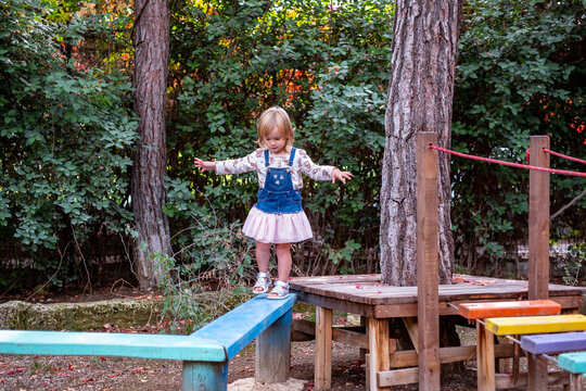 girl walking on a balance log in an outdoor playground in the park 