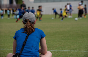 Mom sitting and watching her son playing football in a school football tournament on a sideline...
