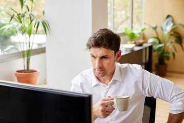 Serious man with coffee working on computer